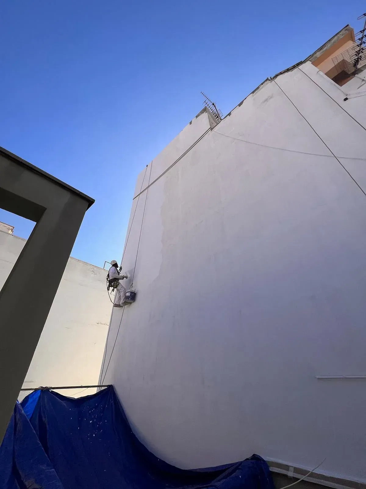 Un hombre está pintando un edificio blanco con una lona azul.
