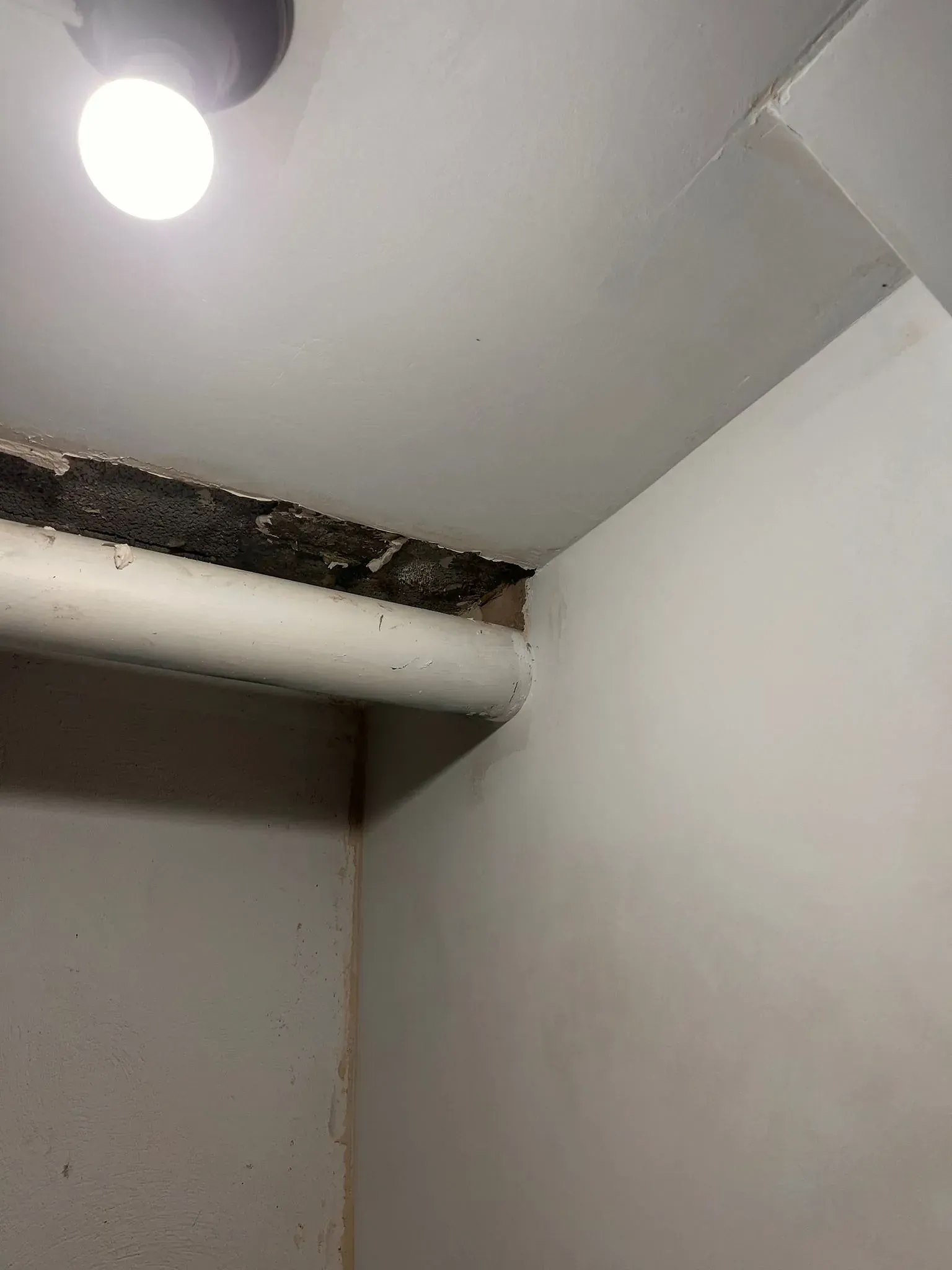 Una pared blanca con una tubería que sale de ella y una luz en el techo.