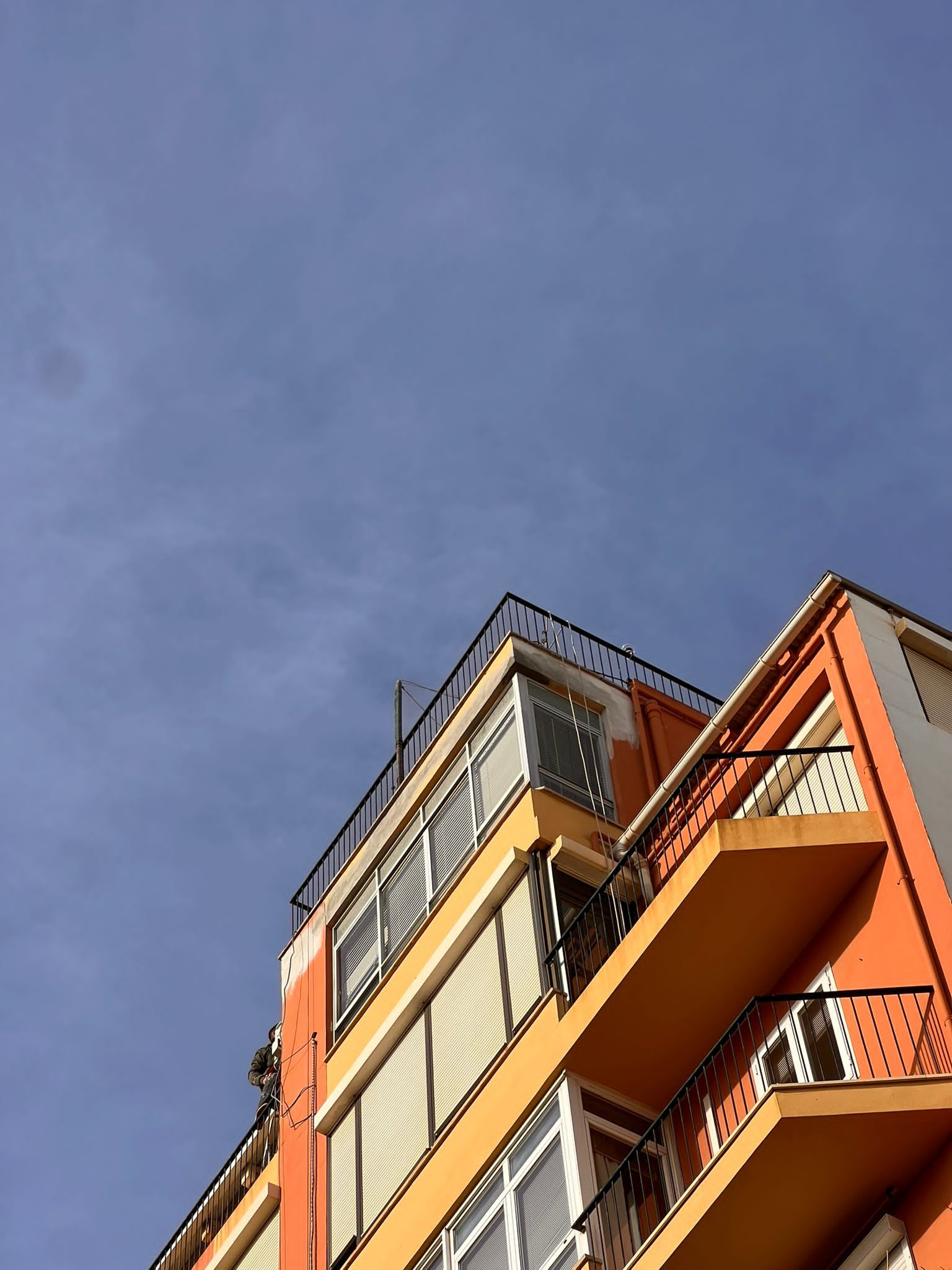 Mirando hacia arriba a un edificio con balcones y un cielo azul al fondo