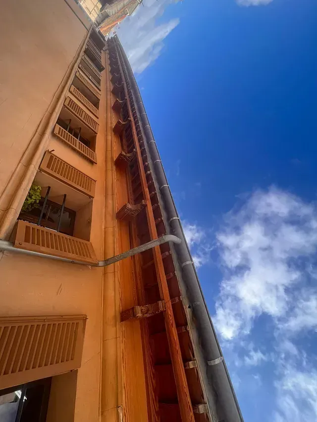 Mirando hacia arriba a un edificio alto con balcones y un cielo azul en el fondo.