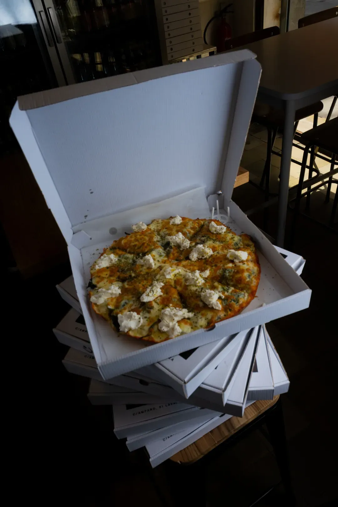 Pizza en una caja abierta encima de una pila de cajas de pizza cerradas, en un restaurante.