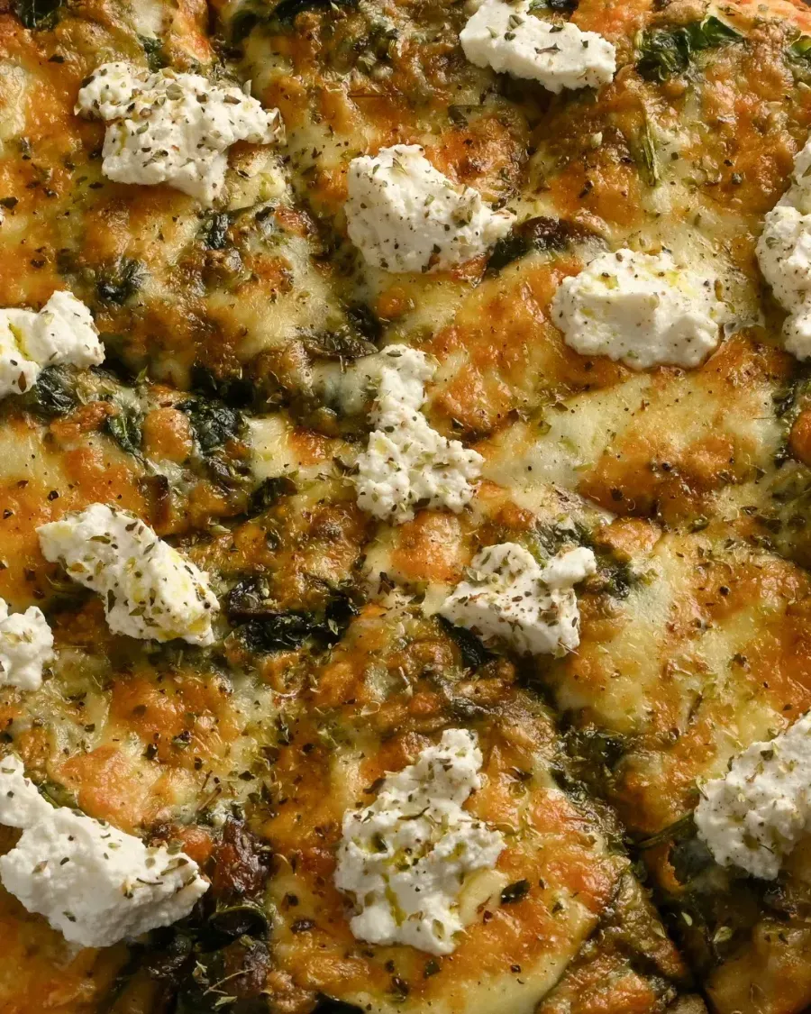 Primer plano de una pizza cubierta con queso y trozos de queso blanco.