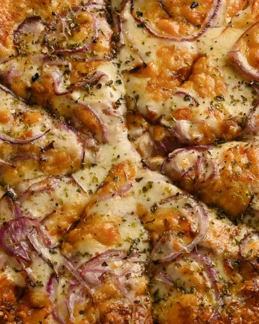 Pizza cubierta con queso derretido y rodajas de cebolla roja.