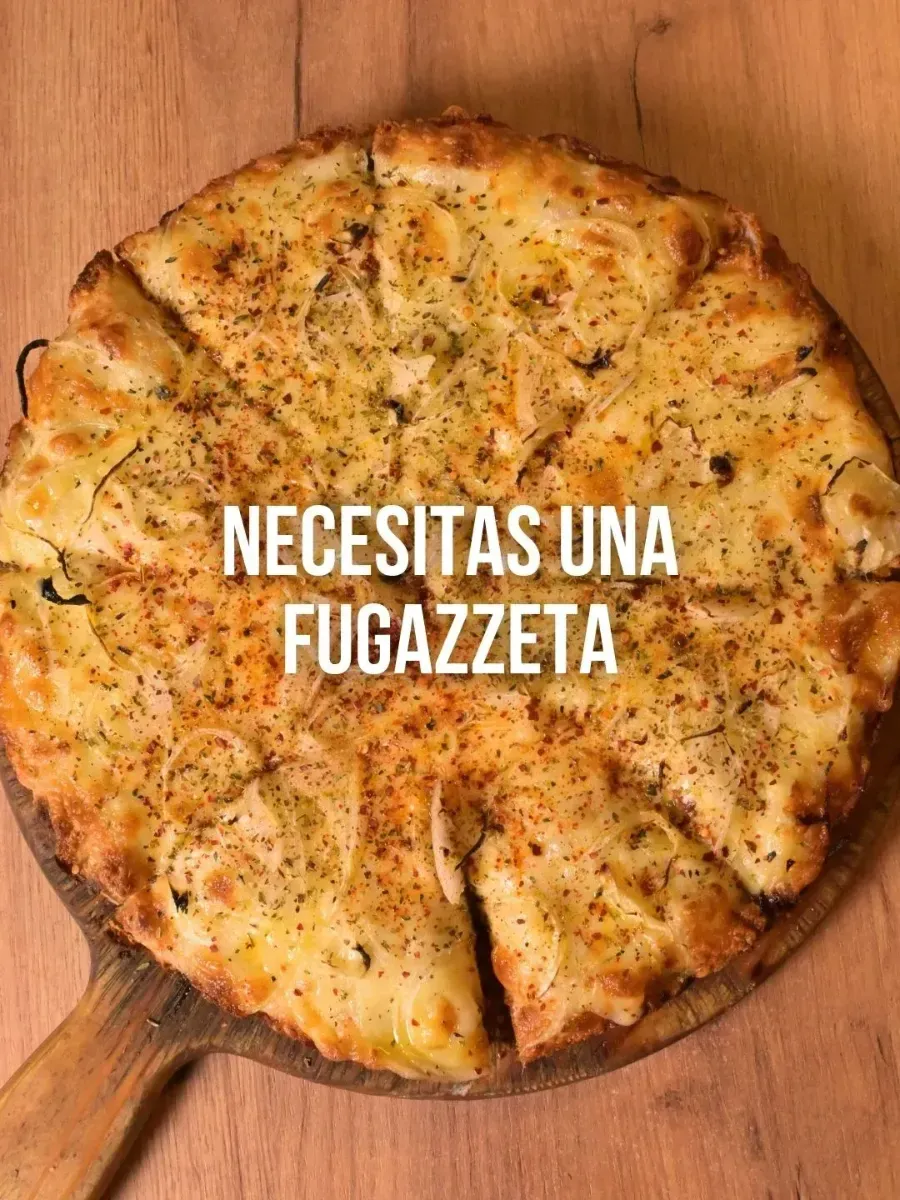 Una pizza fugazzeta horneada, cortada en rebanadas, sobre una tabla de madera. El texto dice: