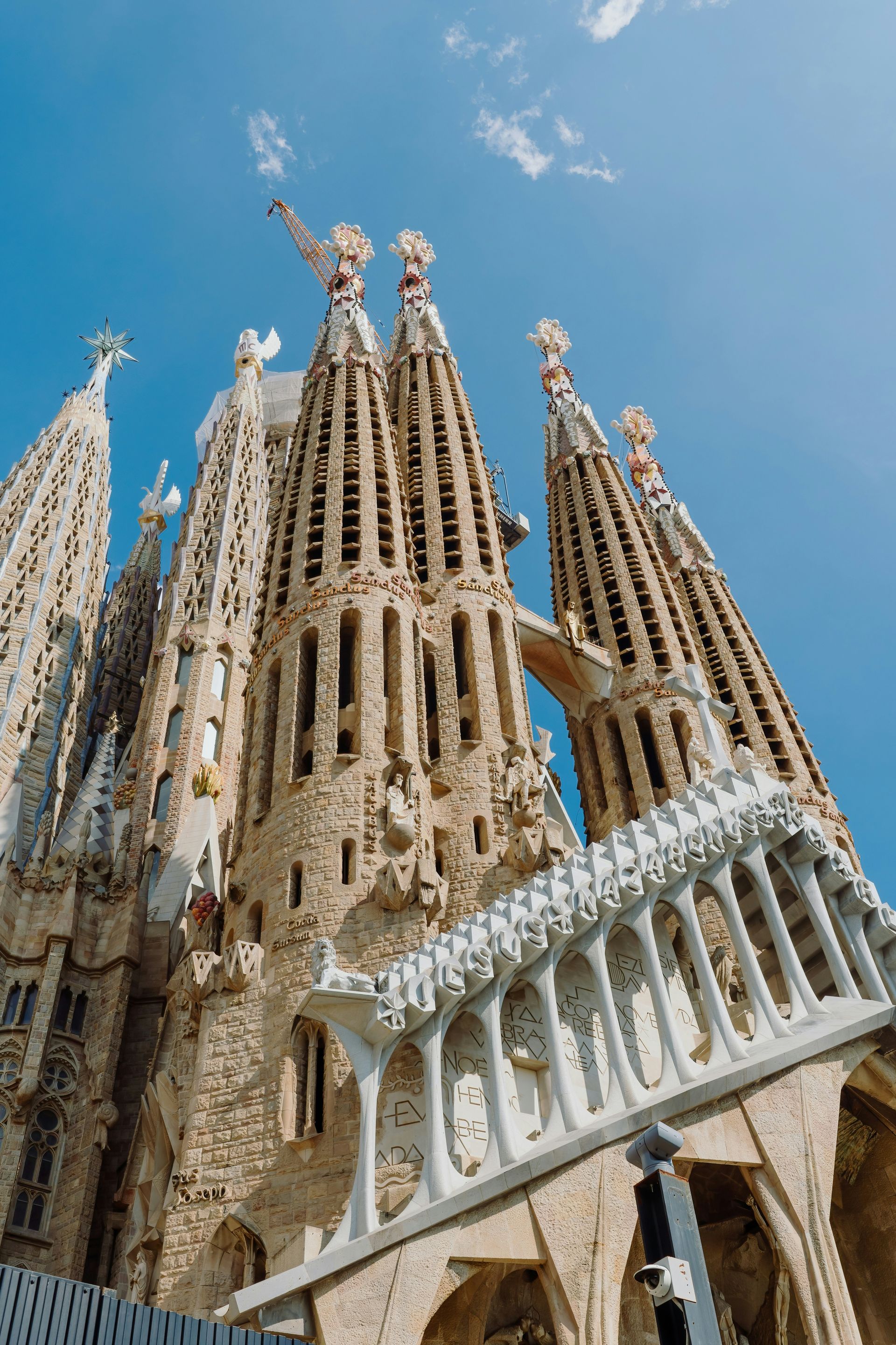Torres catedralicias de estilo Gaudí con agujas ornamentadas contra un cielo azul, vistas desde abajo.