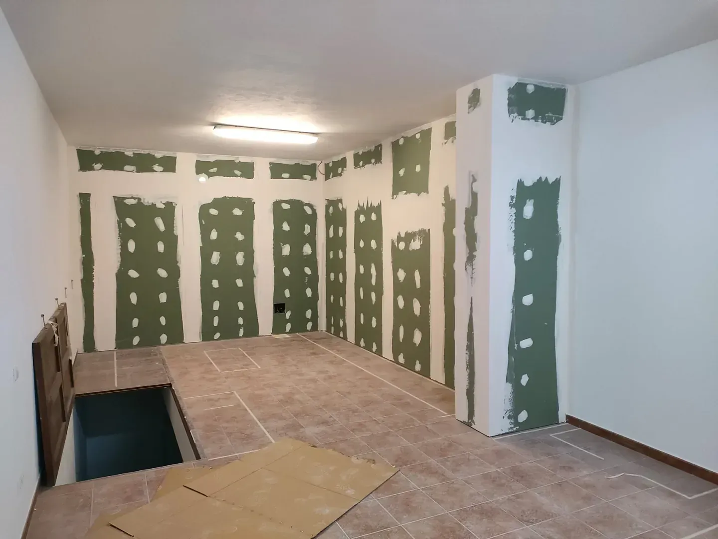 Habitación en construcción; paneles de yeso instalados en paredes y columna de soporte, con piso parcialmente colocado.