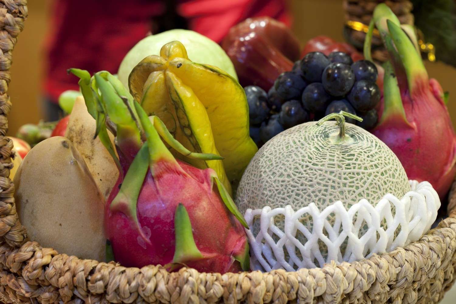 Cesta de frutas tropicales coloridas que incluyen fruta del dragón, uvas y melón.