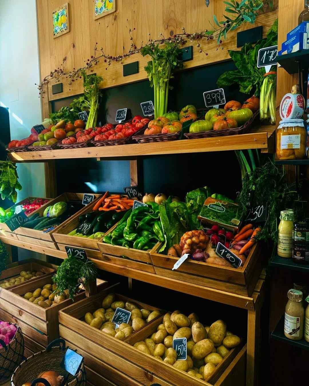 Estantes de madera que muestran productos frescos en un entorno de mercado: tomates, apio, pimientos, zanahorias y patatas.
