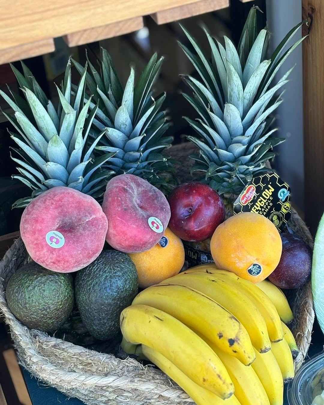 Cesta de frutas variadas: piñas, melocotones, naranjas, plátanos, aguacates.
