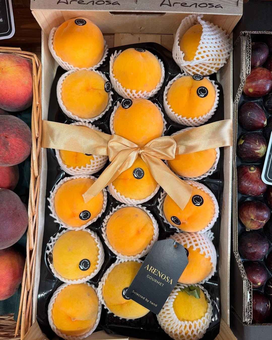 Caja de madera con melocotones amarillos, envueltos individualmente y atados con una cinta dorada.
