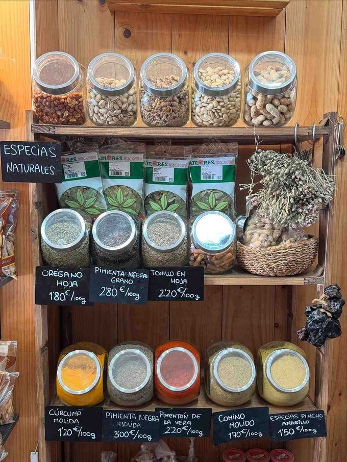 Estantes de especias en frascos. Las especias incluyen frutos secos, hierbas y polvos con etiquetas en español.