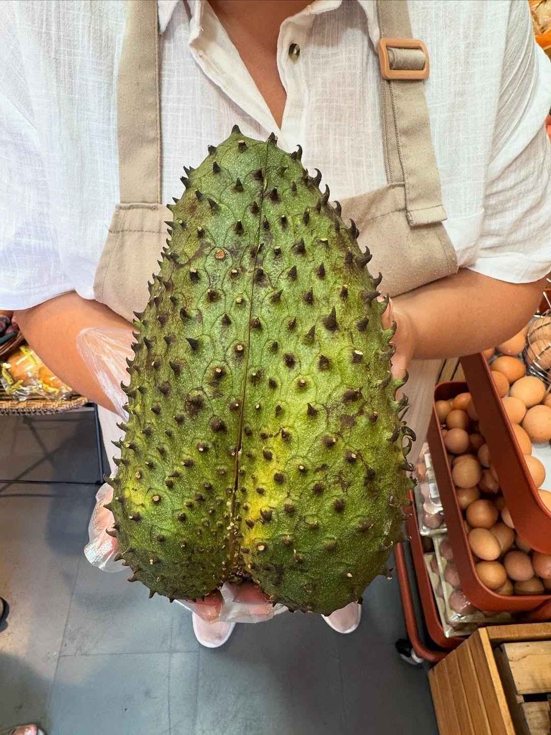 Persona que sostiene un fruto grande de guanábana verde cubierto de protuberancias puntiagudas; usa guantes y delantal.