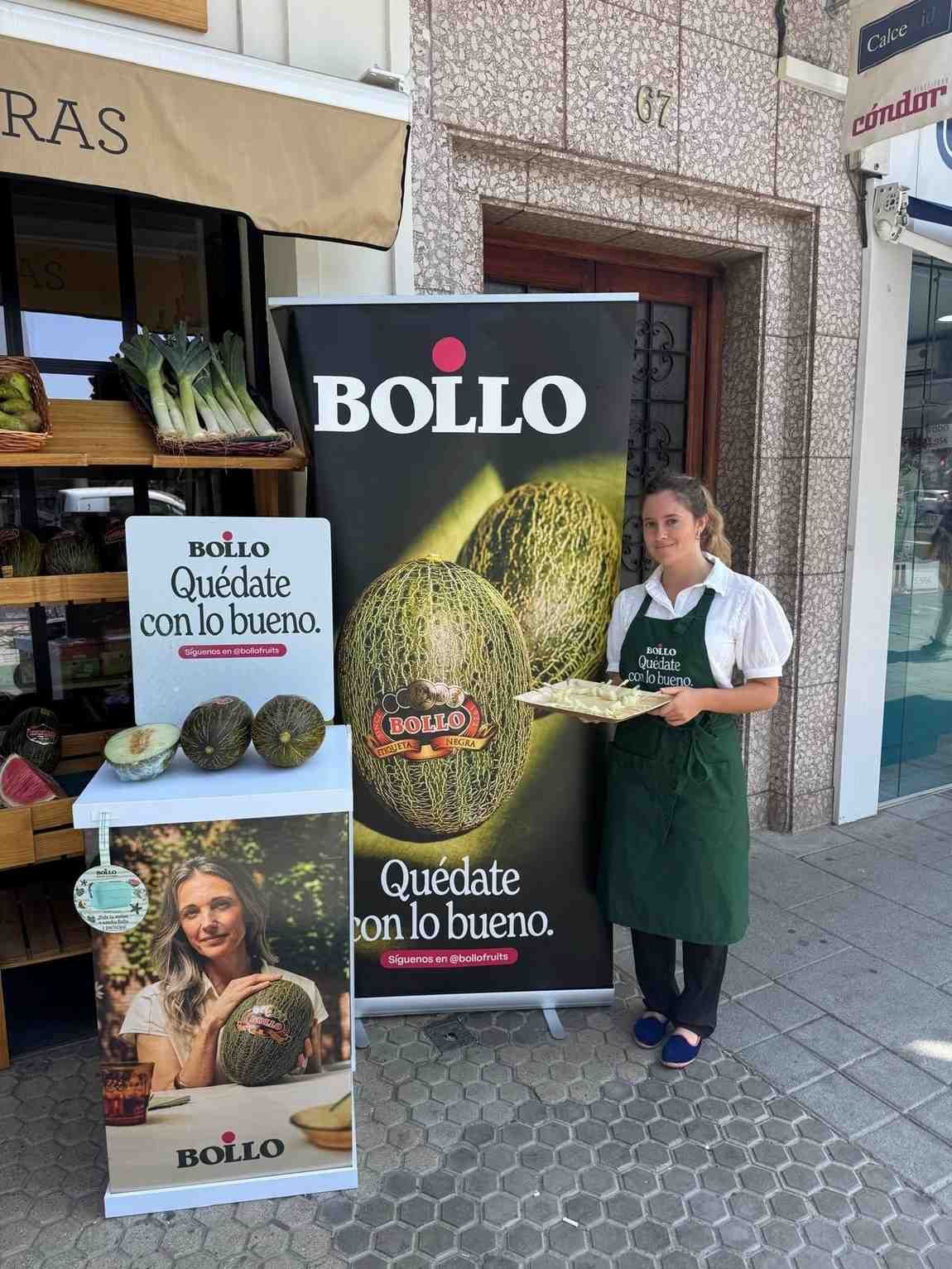 Una mujer con delantal sostiene melones cerca de un cartel promocional de