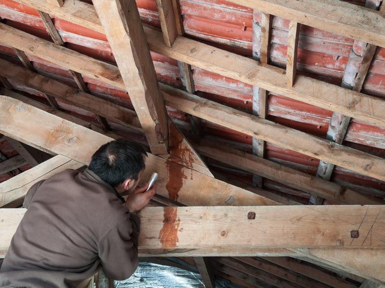 Un homme travaille sur une structure en bois sous un toit.