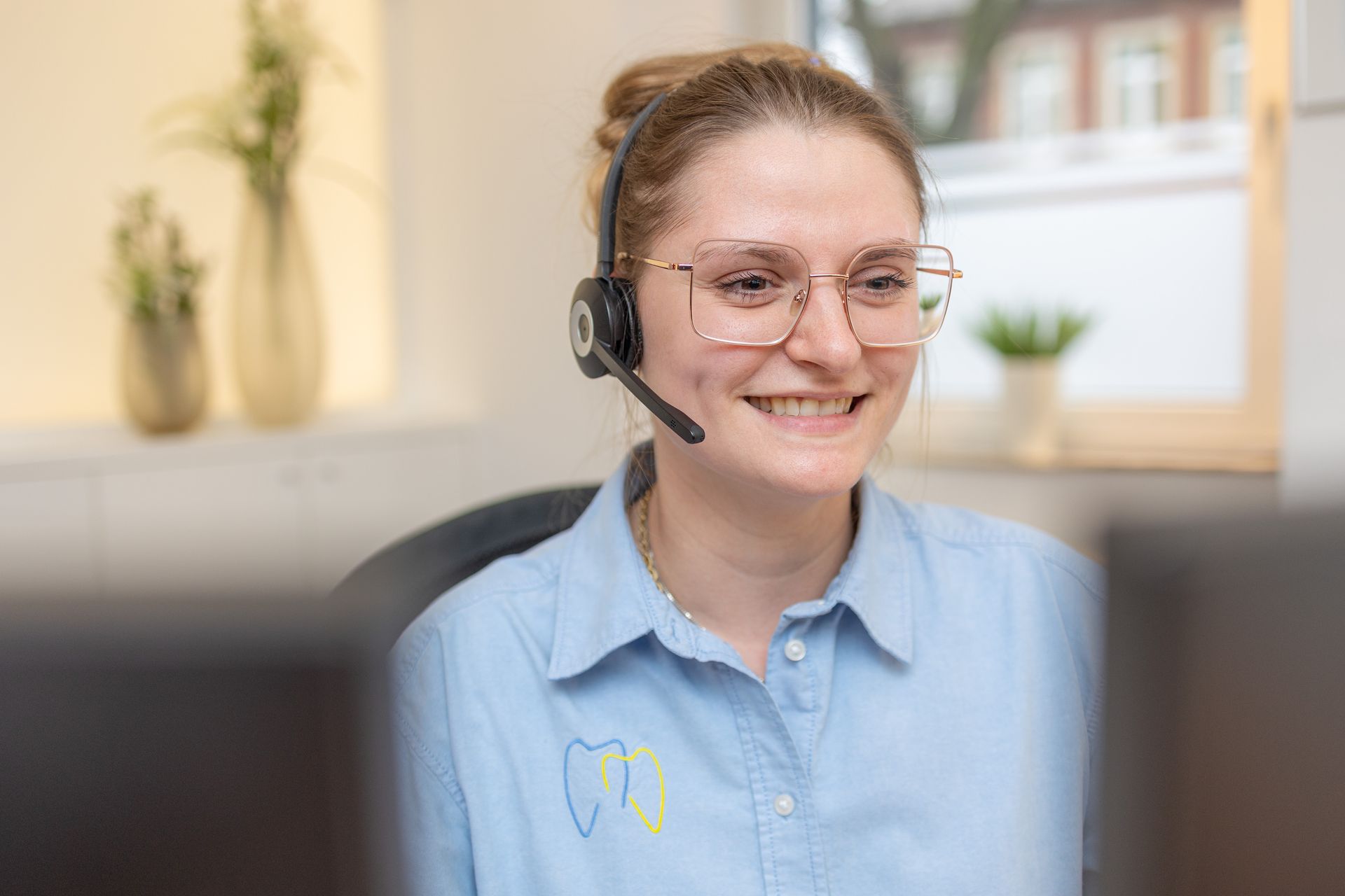 Frau mit Headset lächelt, während sie im Büro an einem Computer arbeitet.