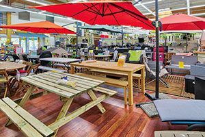 Magasin de meubles d'intérieur, parasols rouges et orange au-dessus de tables et de chaises d'extérieur.