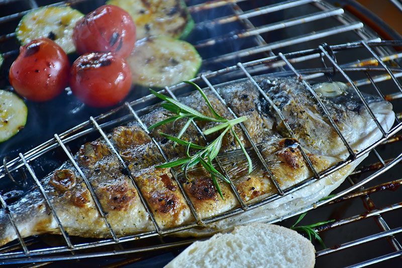Poisson grillé avec des légumes et du romarin sur un gril.