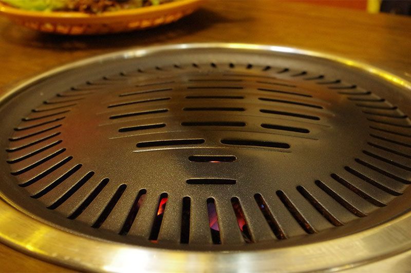 Gros plan sur un barbecue coréen dont la surface est chaude et les braises incandescentes visibles.
