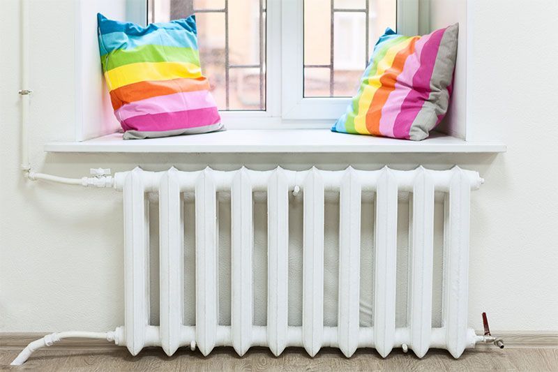 Radiateur blanc sous un rebord de fenêtre avec deux coussins à rayures arc-en-ciel.