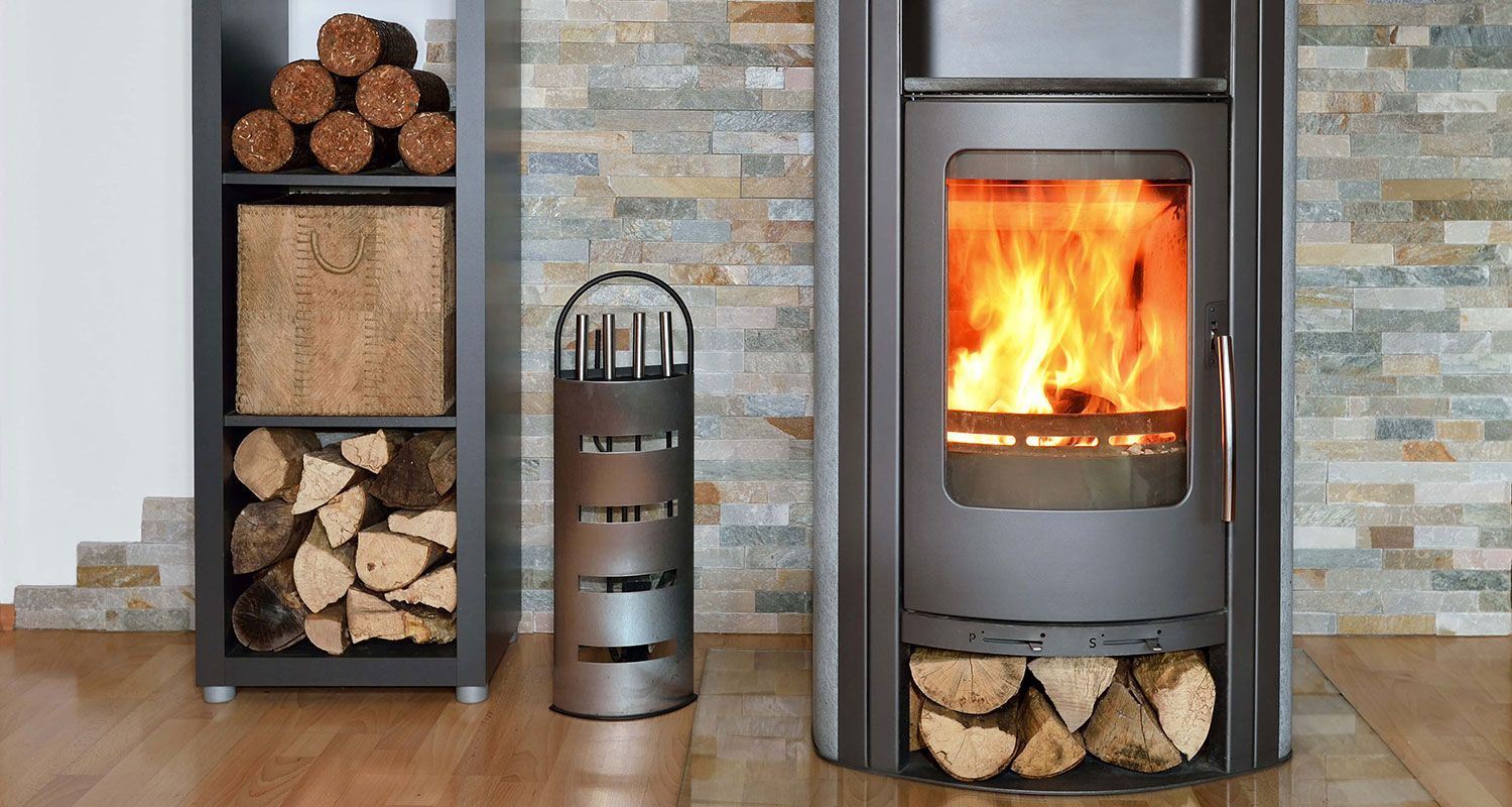Cheminée avec flammes ardentes, rangement pour le bois et panier à bois contre un mur de pierre.