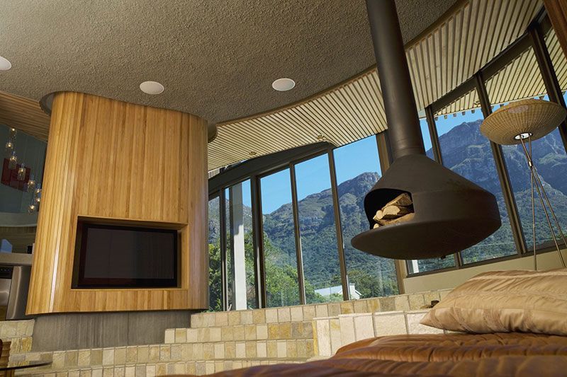 Intérieur moderne avec cheminée suspendue, télévision et grandes fenêtres donnant sur les montagnes.