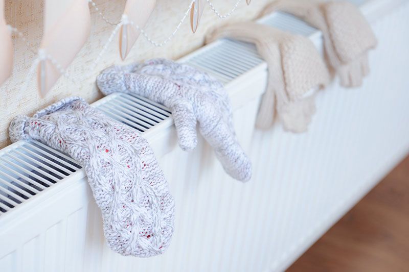 Des moufles et des gants sèchent sur un radiateur blanc.