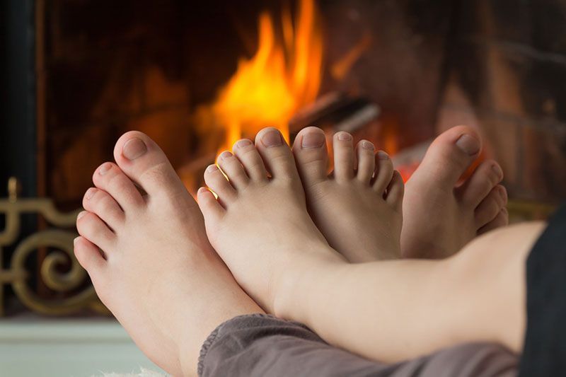 Des pieds posés devant une cheminée avec des flammes qui brûlent en arrière-plan.