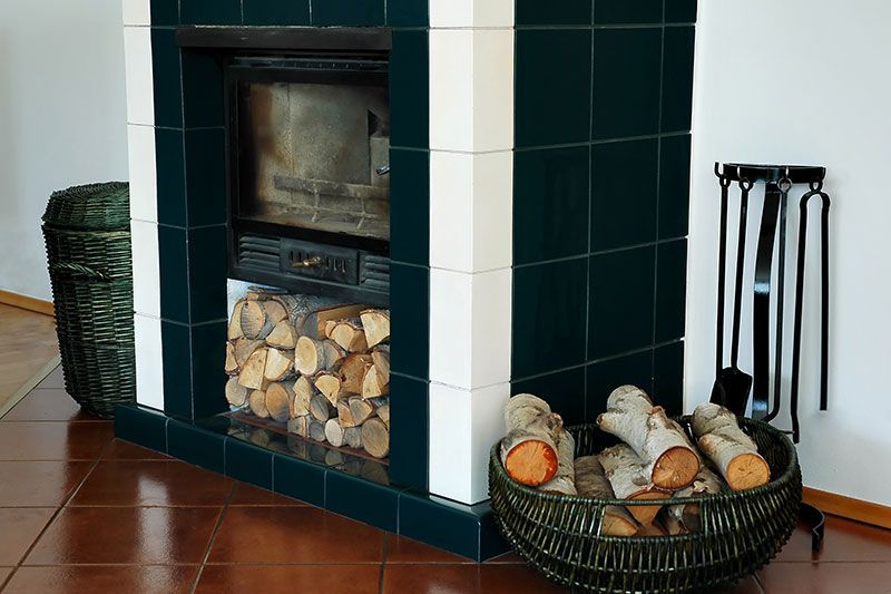 Cheminée avec entourage en carrelage vert, bois de chauffage et accessoires de cheminée.