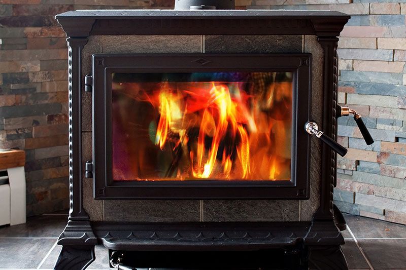 Poêle à bois dont les flammes sont visibles derrière une porte vitrée, adossé à un mur de pierre et de briques.
