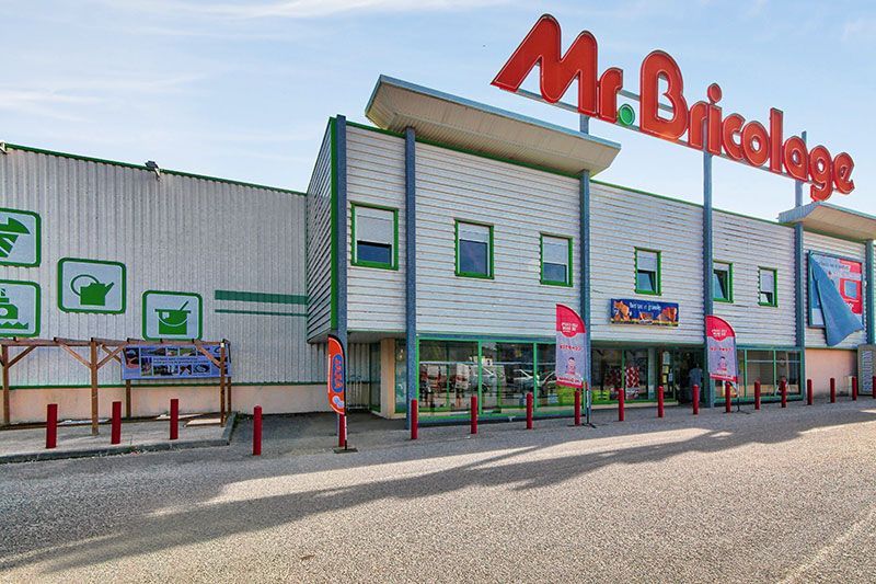 Extérieur du magasin de bricolage Mr. Bricolage ; bâtiment vert et blanc avec enseigne rouge, ciel bleu.