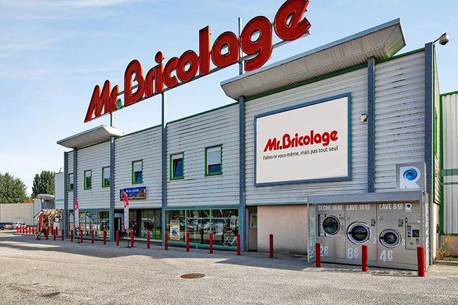 Façade du magasin de bricolage Mr. Bricolage avec enseigne rouge et laverie automatique sur le côté.