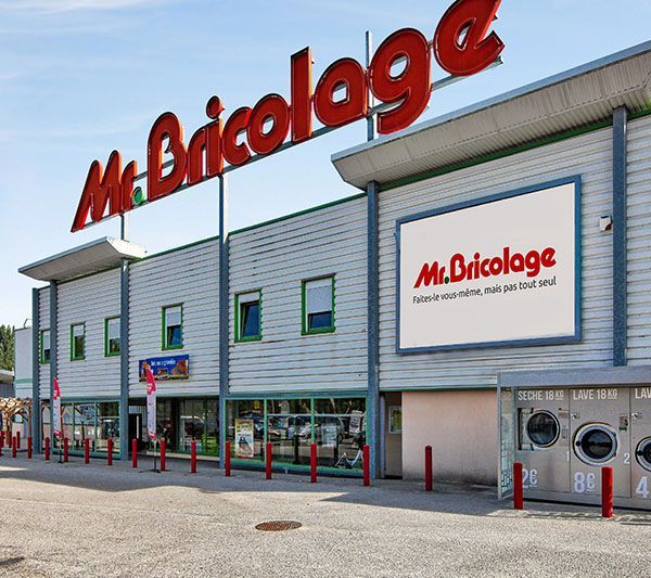 Façade du magasin Mr. Bricolage avec enseigne rouge et façade bleu clair. Journée ensoleillée.