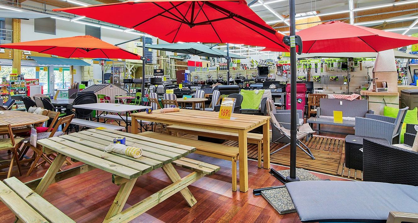 À l'intérieur d'un magasin : présentation de mobilier d'extérieur avec des parasols rouges et oranges.