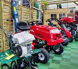 Tondeuses à gazon exposées dans un magasin : une tondeuse autoportée rouge et des tondeuses à pousser plus petites.