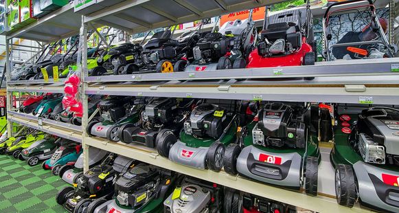 Des rangées de tondeuses à gazon de différentes couleurs et de différents modèles sont exposées sur les étagères d'un magasin.