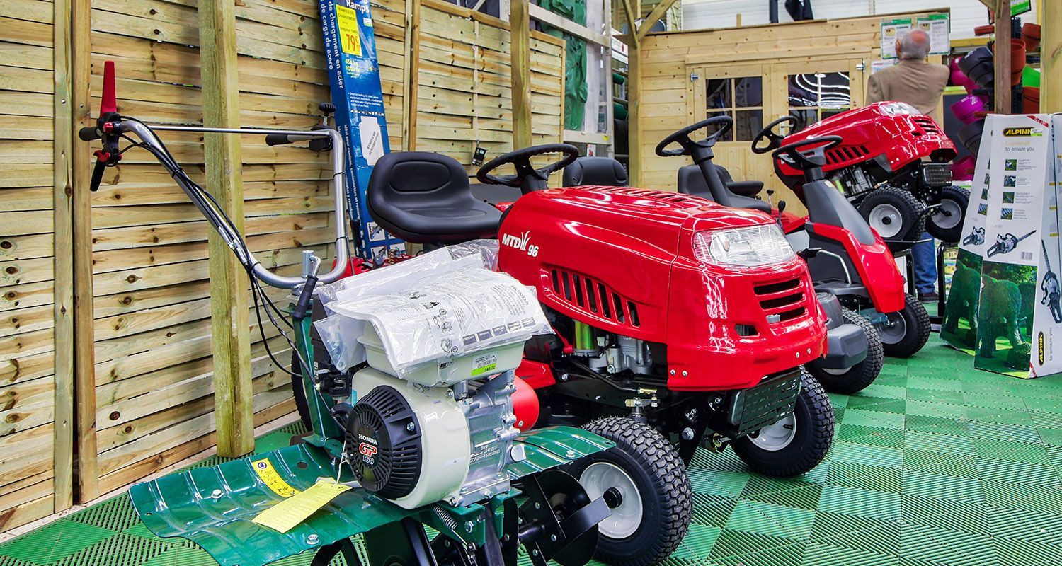Présentation de tracteurs de pelouse rouges et d'une motobineuse dans un magasin de bricolage.