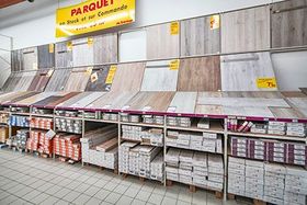 Des échantillons de parquet sont exposés dans un magasin, avec des étagères remplies de revêtements de sol emballés en dessous.