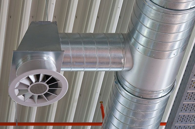 Système de ventilation argenté sur un plafond blanc ondulé. Grille d'aération circulaire à ailettes réglables.