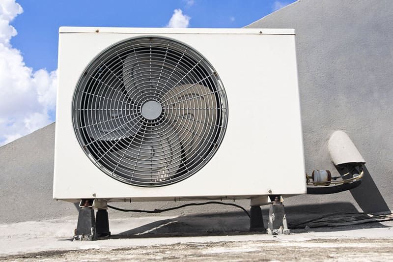 Unité de climatisation blanche avec un grand ventilateur sur un toit, se détachant sur un ciel bleu.