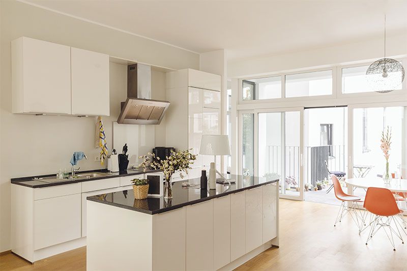 Cuisine blanche avec îlot central et plan de travail noir. Espace lumineux et moderne avec coin repas apparent.