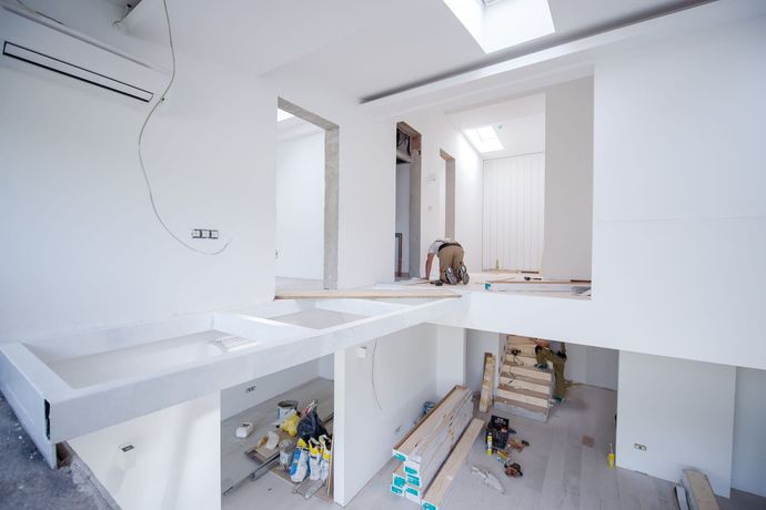 Interior blanco luminoso en proceso de renovación con suelo abierto, escaleras y materiales de construcción alrededor de un espacio tipo loft.
