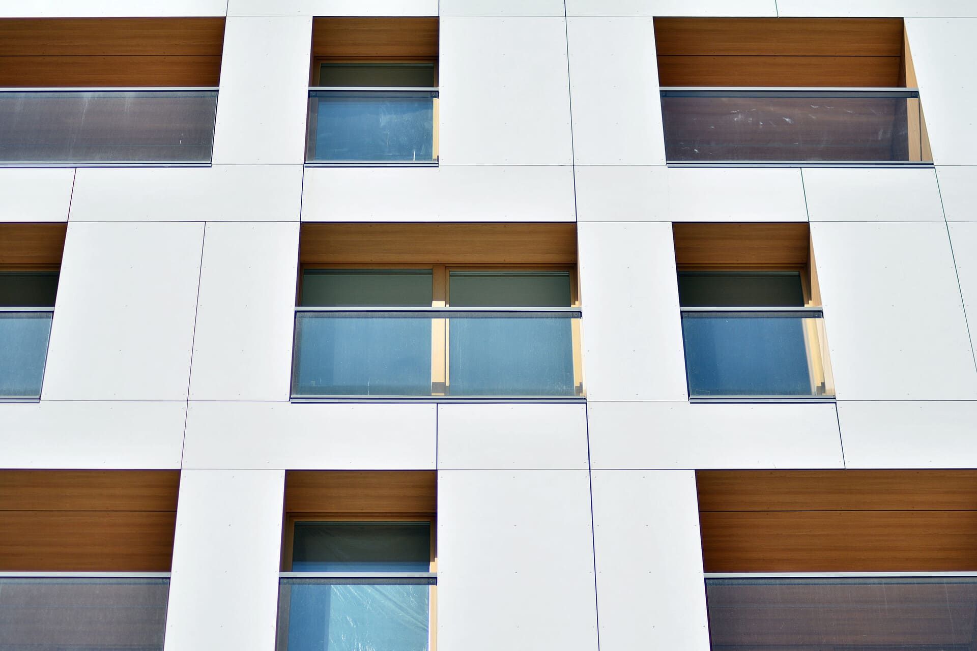 Fachada de edificio moderno con paneles blancos, ventanas tintadas de azul y detalles de madera.