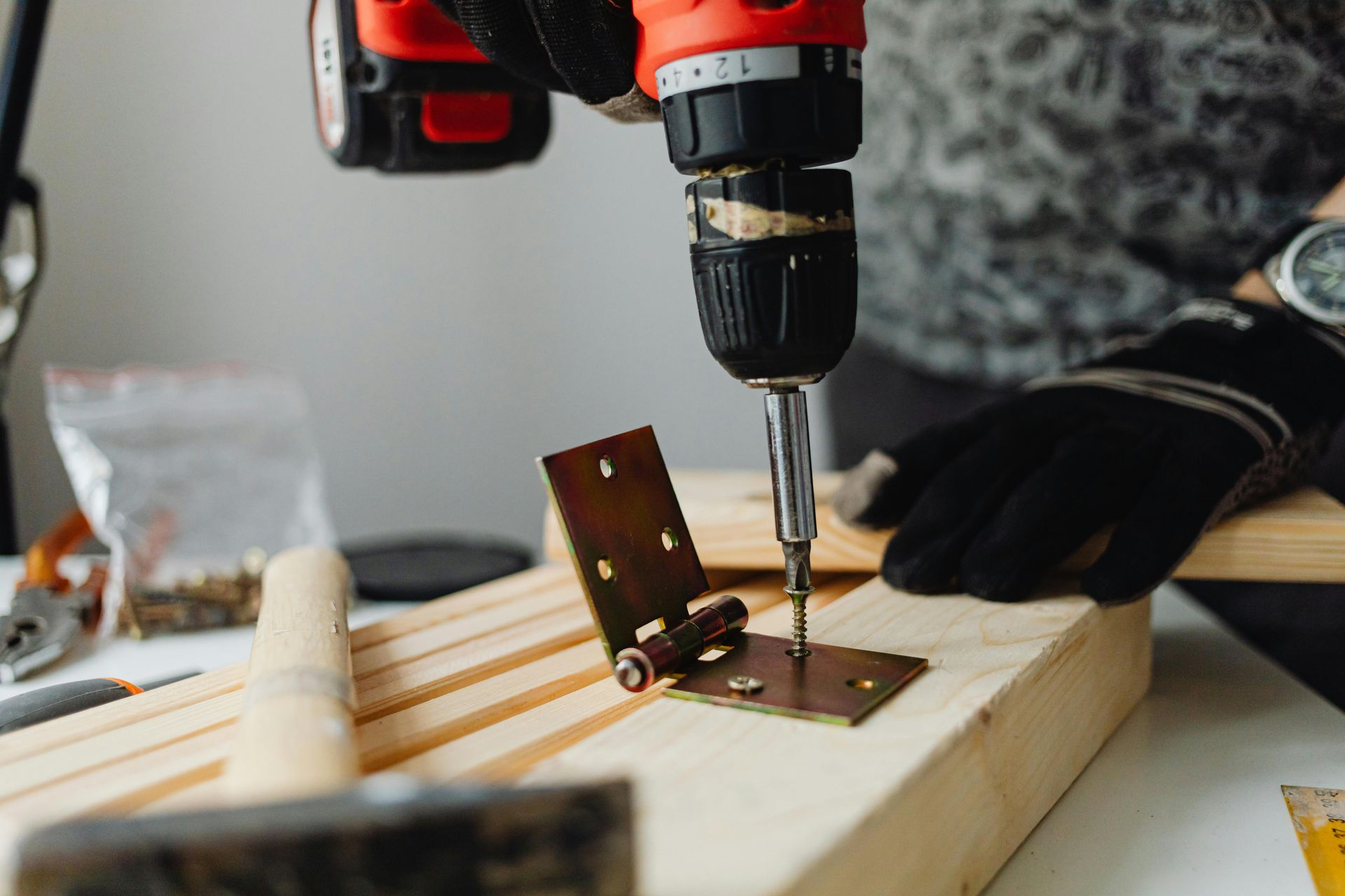 Manos utilizando un taladro para fijar un soporte metálico a una tabla de madera sobre un banco de trabajo.