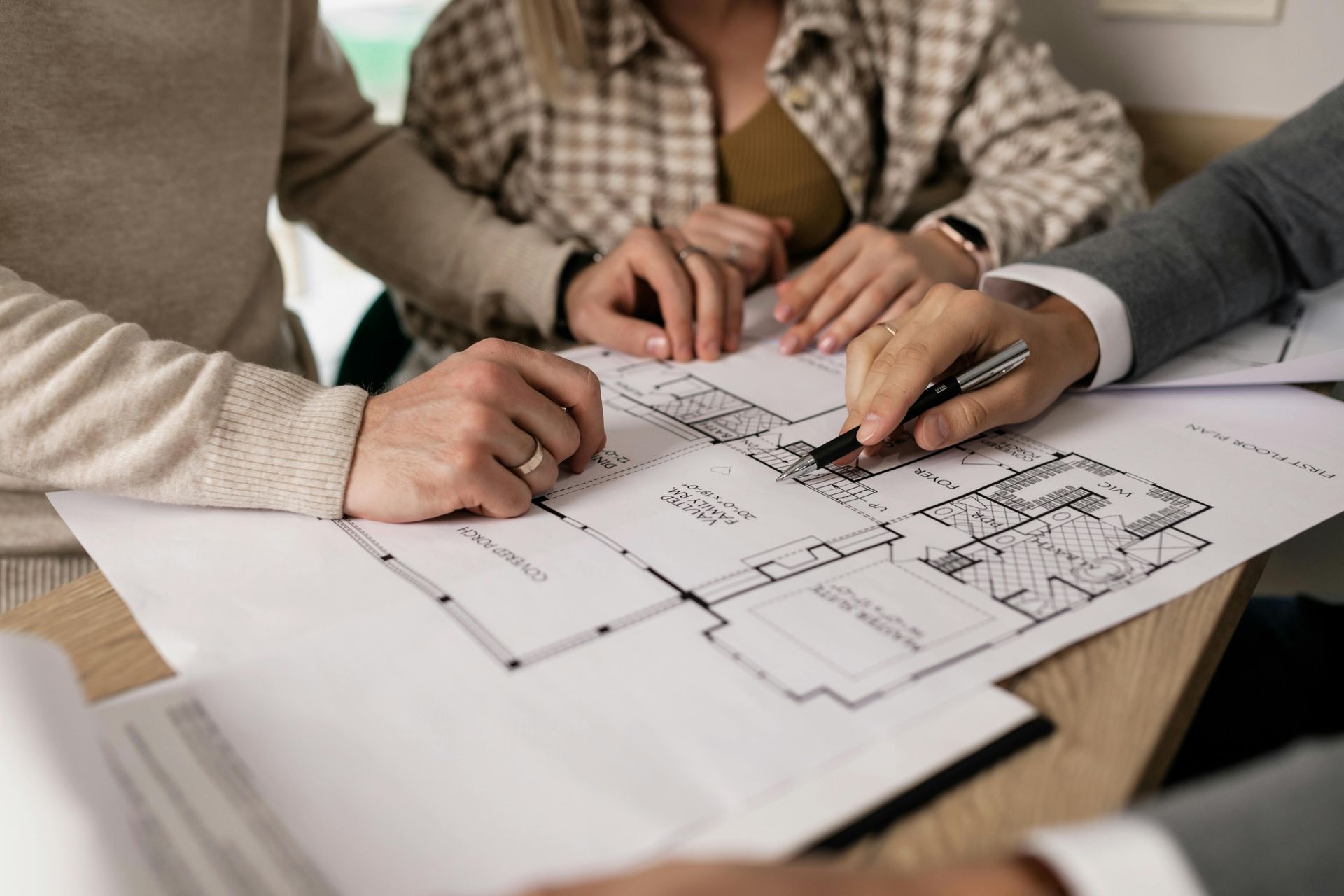 Manos señalando un plano arquitectónico sobre una mesa durante una reunión de planificación.
