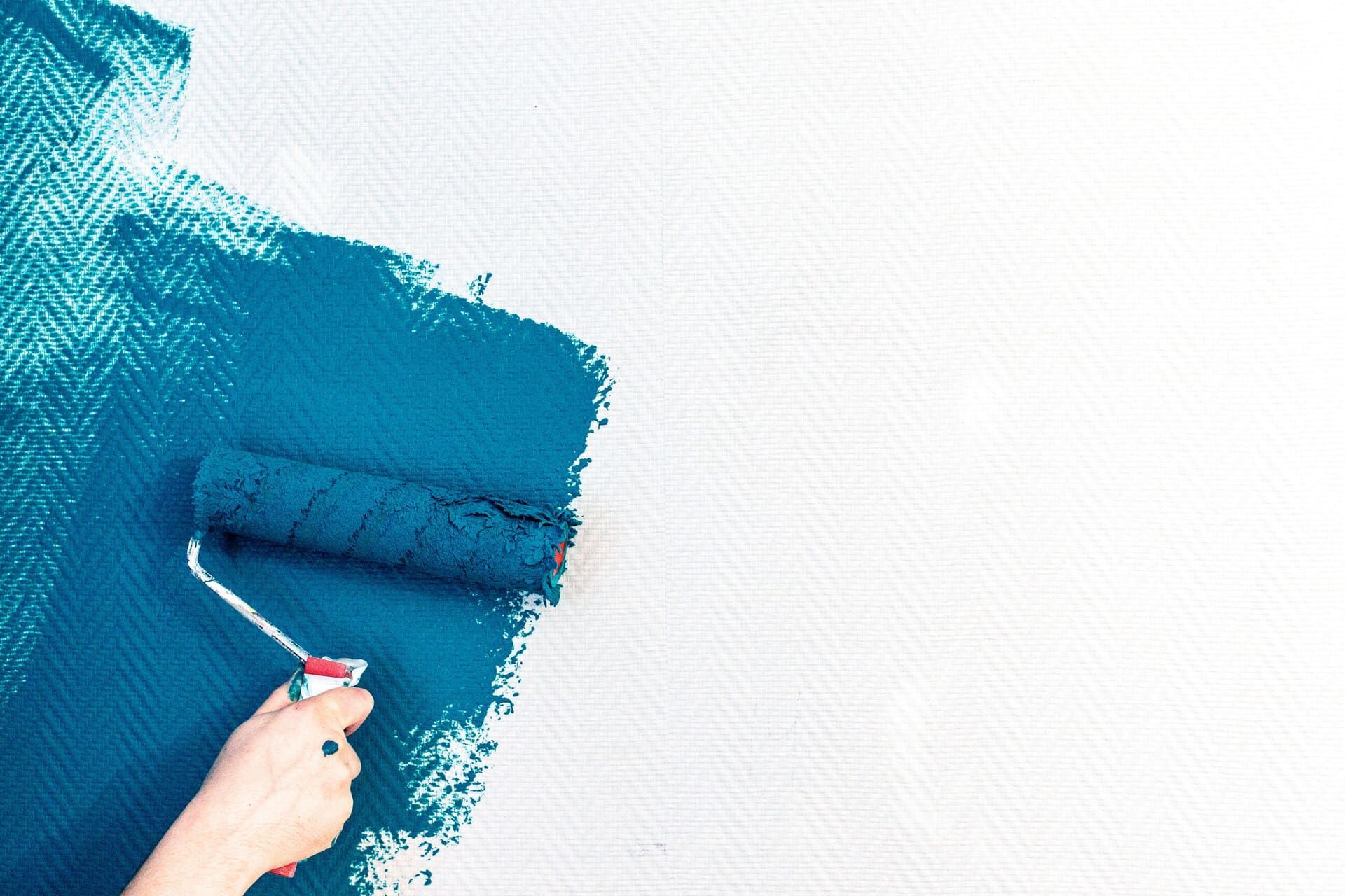 Aplicar pintura azul a mano sobre una pared blanca, creando una superficie pintada con textura.