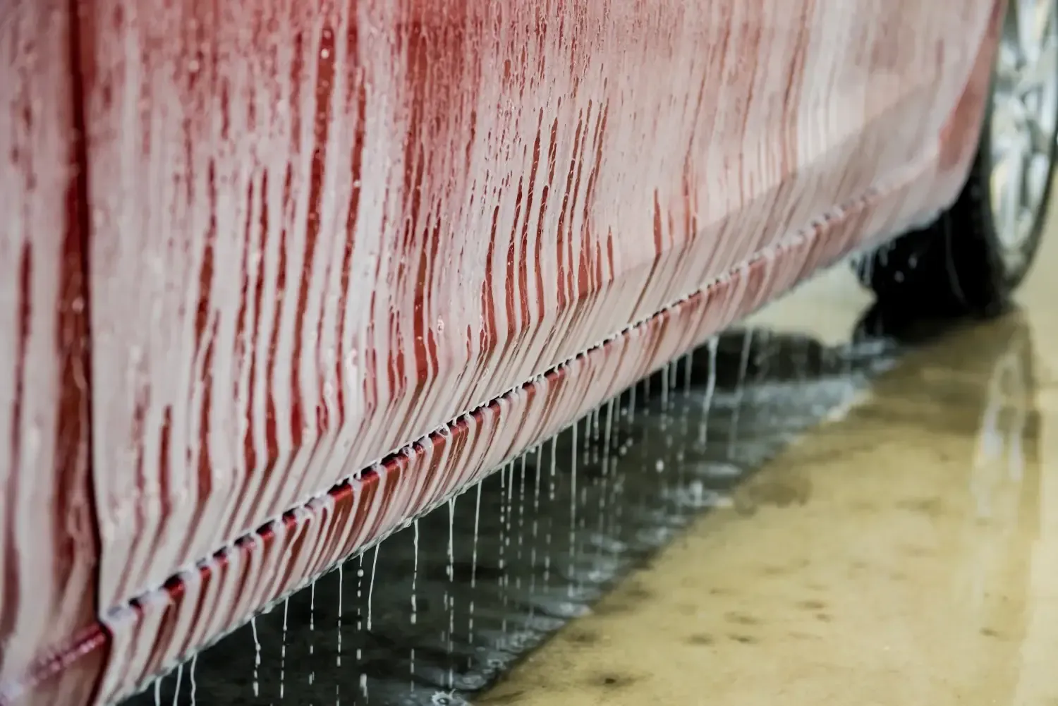 Puerta de coche roja con agua goteando durante un lavado de coche.