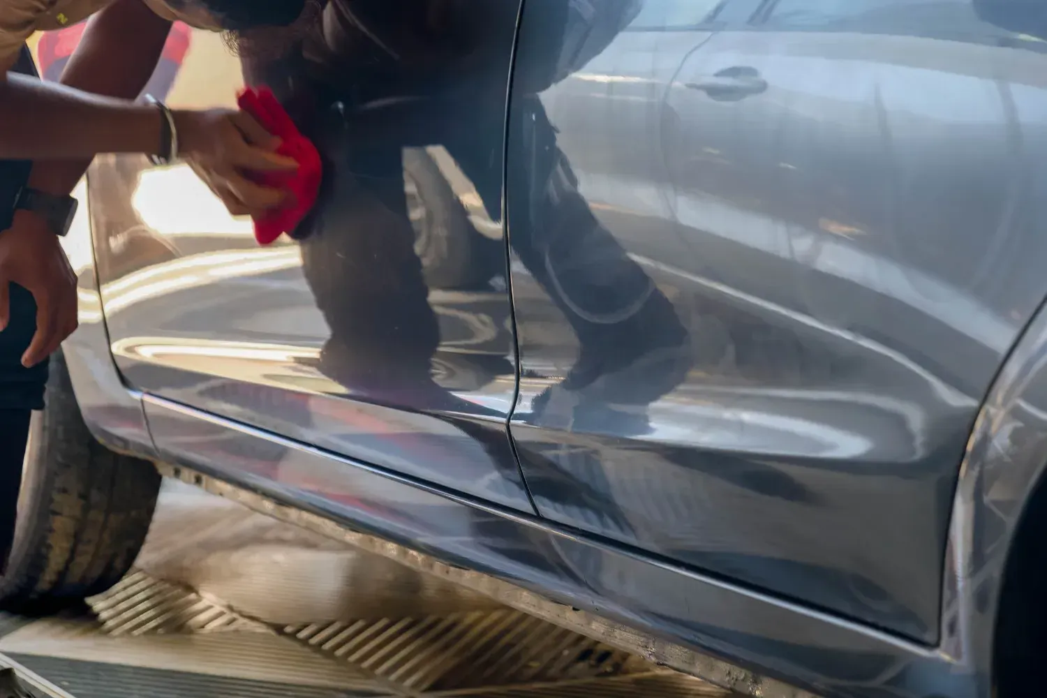 Persona limpiando un coche gris brillante con un paño rojo.