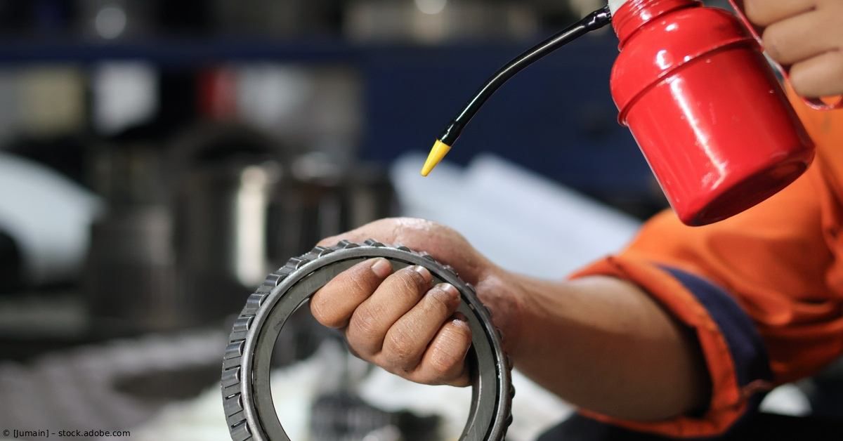 Ein Arbeiter untersucht in einer Werkstatt einen Metallring mit einer roten Werkzeugmaschine.