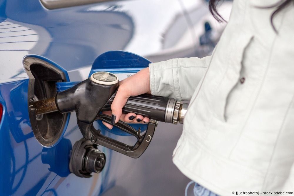 Eine Hand hält eine Zapfpistole und betankt ein blaues Auto an einer Tankstelle.