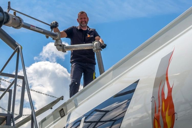 Ein Arbeiter befestigt auf einem Dach unter blauem Himmel ein Metallrohr neben Solarmodulen.